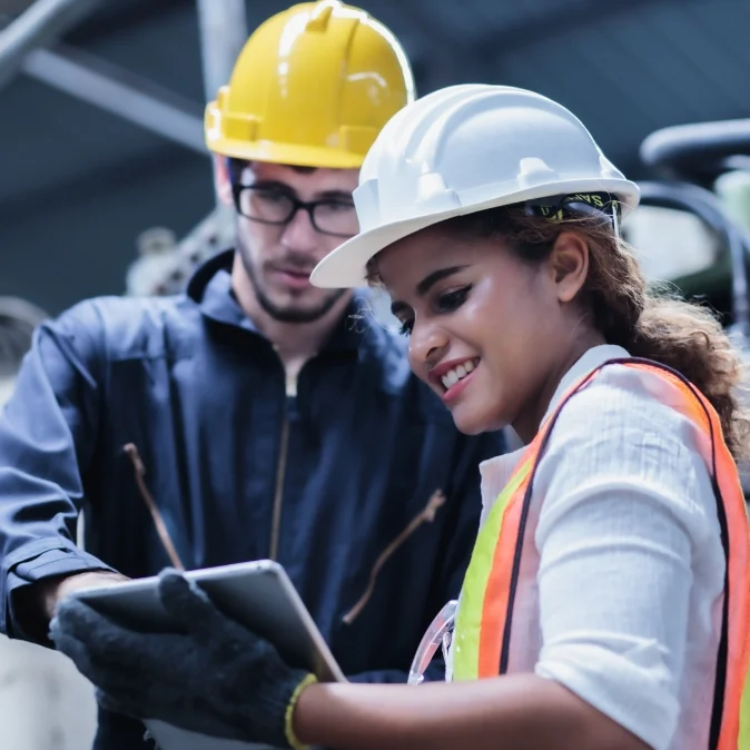 Two people in hard hats reviewing information on a notepad